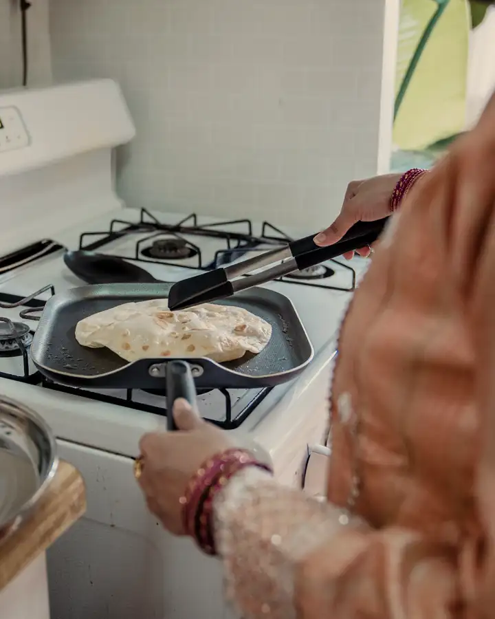 A woman in a kurta making rotis on a gas stove at home